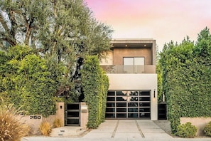 A modern two-story building with a garage, surrounded by dense greenery.