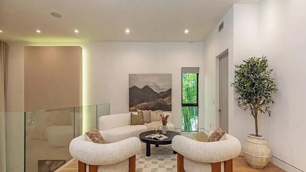 Un salon moderne avec une balustrade en verre, un canapé, deux fauteuils, une table basse et une grande plante en pot.