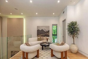 A modern living room with a glass railing, a sofa, two armchairs, a coffee table, and a large potted plant.