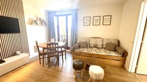 A living room with a wooden floor, a sofa, a dining table with chairs, and a TV mounted on the wall. - Apartment sleeps 6 All comforts, at the foot of the slopes (Montclar)