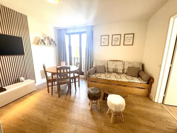Un salon avec un plancher en bois, un canapé, une table à manger avec des chaises et un téléviseur fixé au mur.
