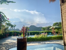 A patio area with a glass table, potted plants, and a view of a pool and mountains.