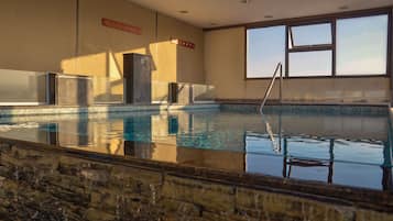 Una piscina techada, una piscina al aire libre, sombrillas