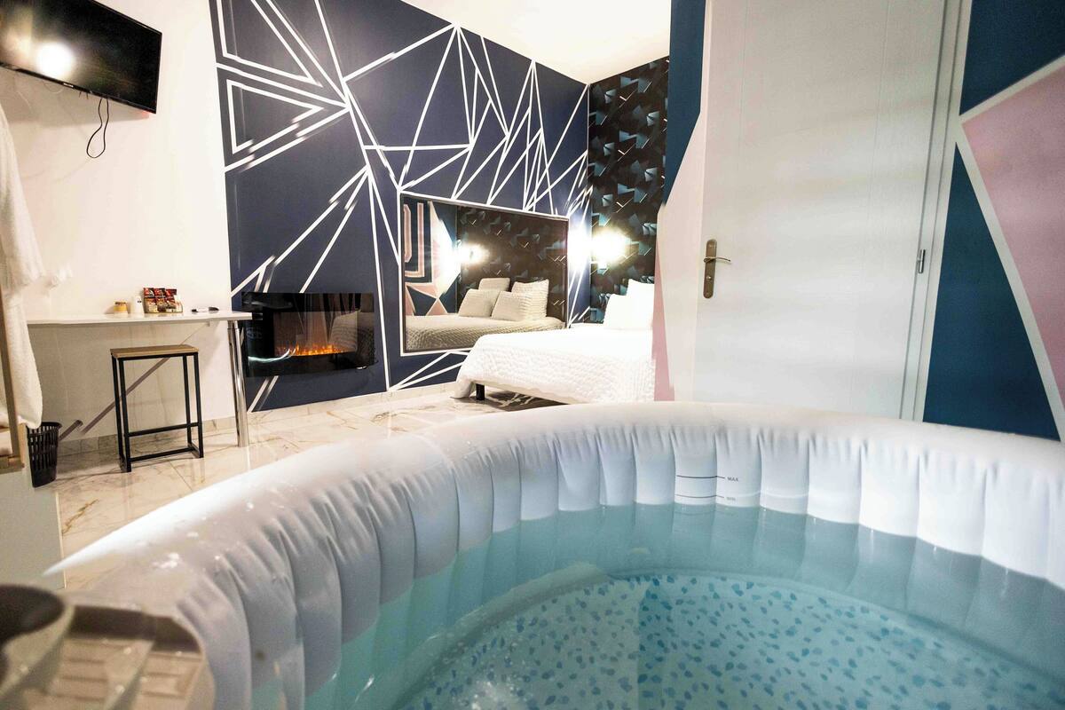 A bedroom with a bed, a small desk, a TV, and a hot tub.