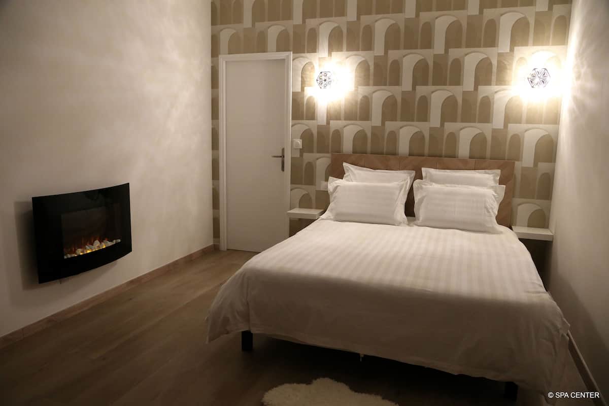 A bedroom with a bed, a wall-mounted fireplace, and patterned wallpaper.
