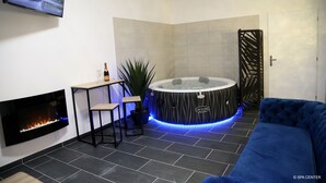 A modern spa area with a fireplace, a hot tub, a sofa, and a TV mounted on the wall. - SPA CENTER Saint-Quentin (Saint-Quentin)