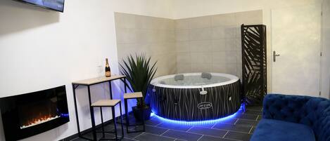 Un moderno espacio de spa con chimenea, jacuzzi, sofá y televisor montado en la pared.