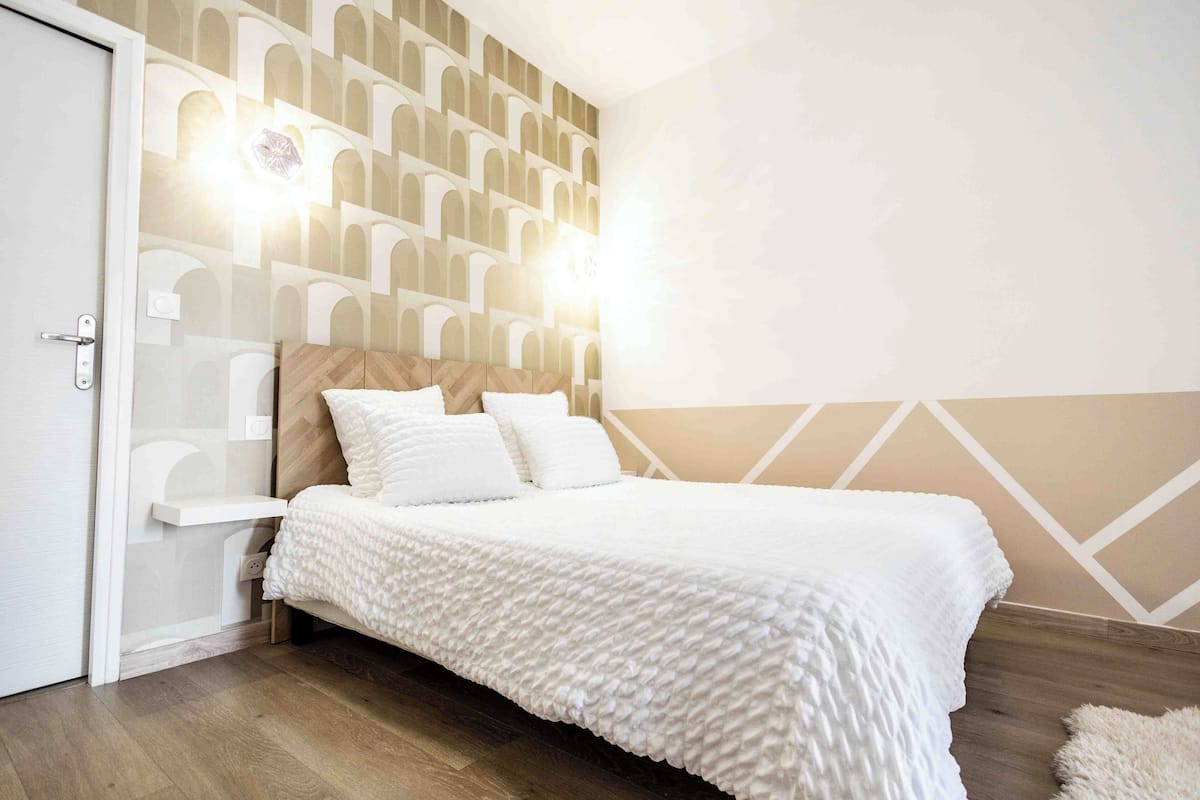 A bedroom with a bed, a nightstand, a wall-mounted light, and a geometric-patterned wall.
