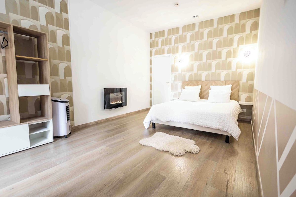 A bedroom with a bed, a white wardrobe, a heater, and a patterned wall.