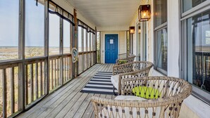 Eine überdachte Veranda mit Korbmöbeln, einer blauen Tür und großen Fenstern.
