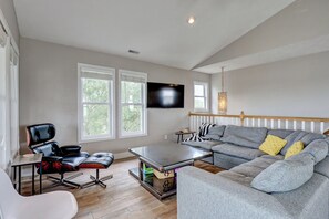 A modern living room with a sectional sofa, a black leather chair, a small table, and a flat-screen TV mounted on the wall.
