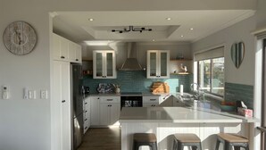 A modern kitchen with white cabinetry, a central island with bar stools, a built-in oven, and a backsplash with teal tiles. - Seabreeze At Shalfleet (Ventnor)