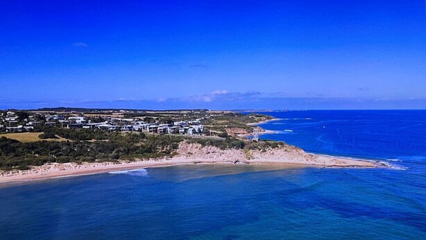 An aerial view of a coastal area with a beach, clear blue waters, and a residential area with houses. - Seabreeze At Shalfleet (Ventnor)