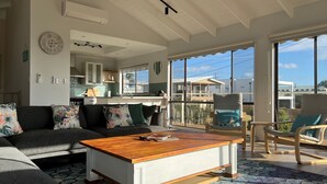 A spacious living room with a wooden coffee table, grey sofa, and teal cushions. A kitchen with a window and a balcony is visible in the background. - Seabreeze At Shalfleet (Ventnor)