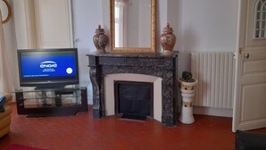 A living room with a fireplace, a television displaying 'ENGIE', and decorative items on the mantel. - Appartement Centre Ville 110m2 (Béziers)