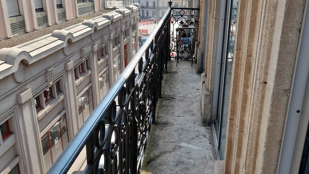A narrow balcony with a black metal railing, overlooking a street with buildings and a parked car. - Appartement Centre Ville 110m2 (Béziers)