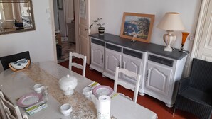 A dining area with a marble table set for four, white chairs, a white cabinet with drawers, a framed painting, and a lamp. - Appartement Centre Ville 110m2 (Béziers)