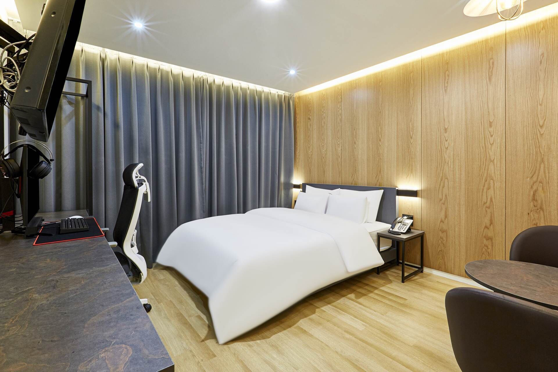 Une chambre d’hôtel moderne, dotée d’un grand lit, d’un bureau avec un ordinateur et des écouteurs, d’une chaise et d’une petite table.