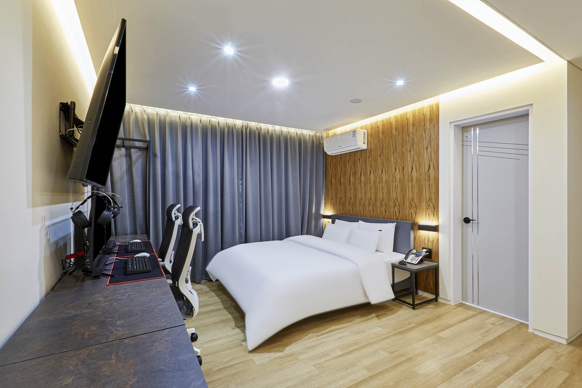 A modern hotel room with a bed, a desk with a computer, a TV, and a pair of skis.
