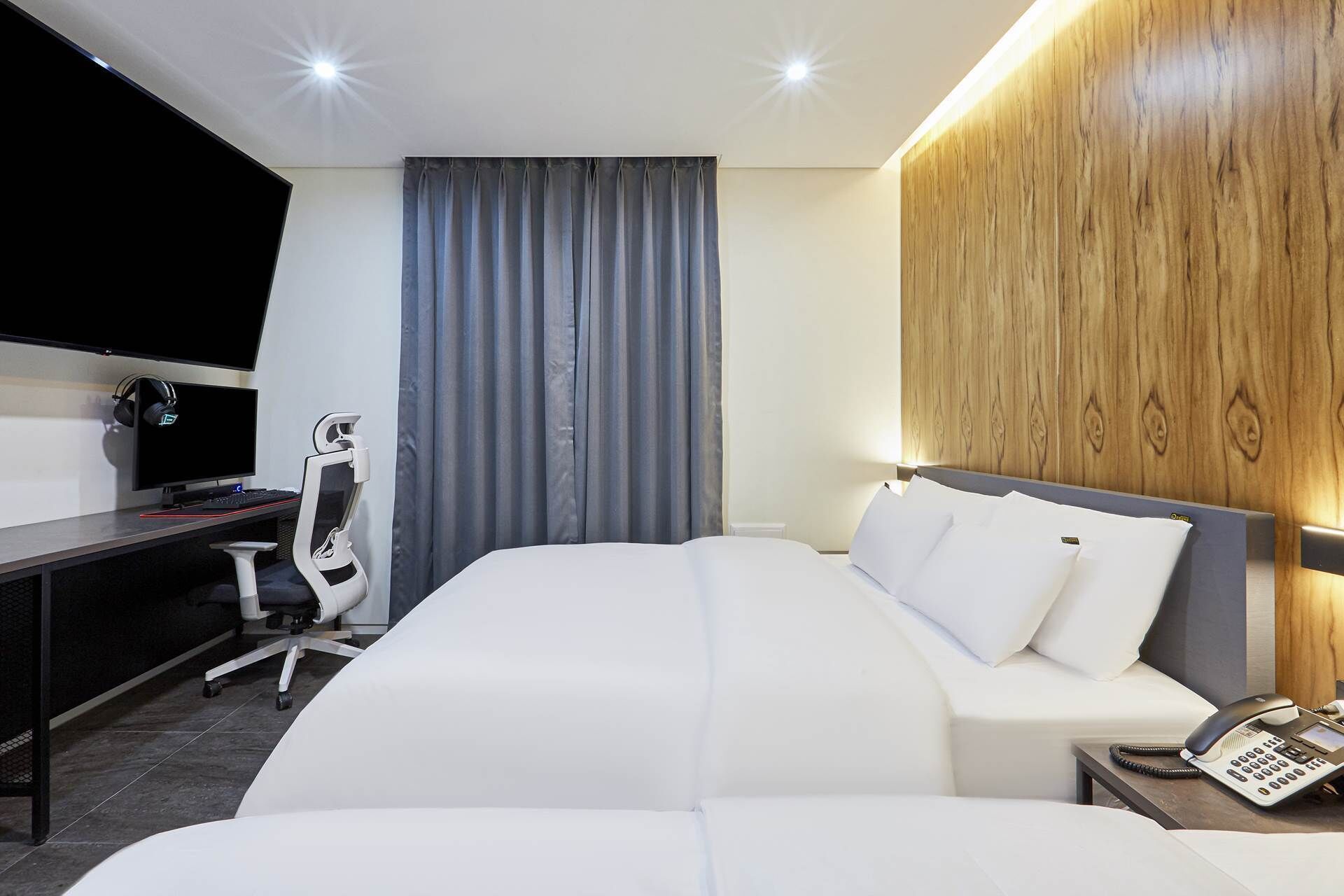 A hotel room with a bed, a desk with a computer, a chair, a telephone, and a television.