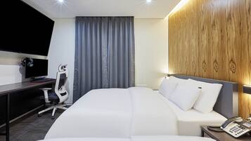 A hotel room with a bed, a desk with a computer, a chair, a telephone, and a television.