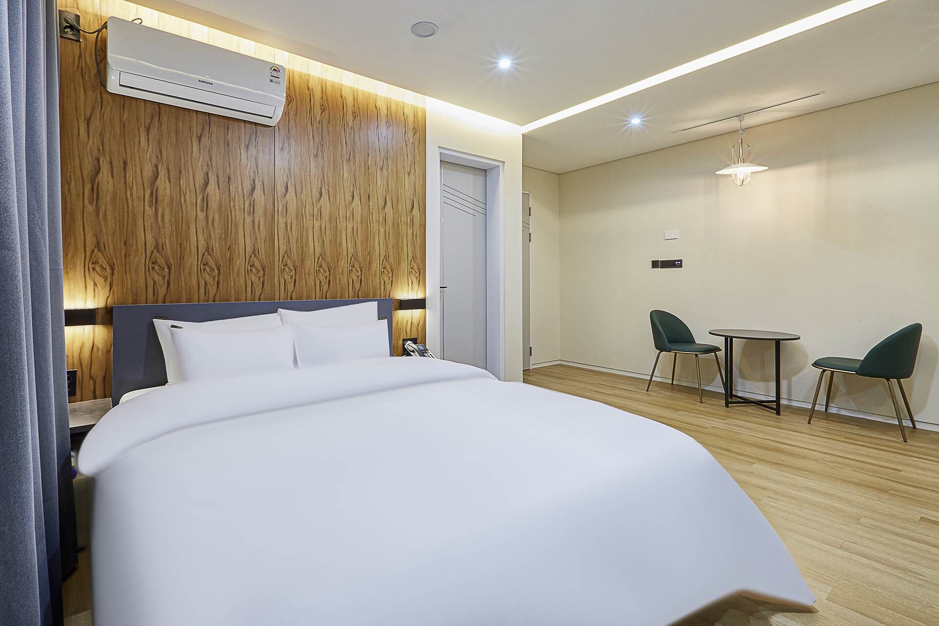 Habitación de hotel con una cama grande, un muro decorativo de madera, una pequeña mesa con dos sillas y una lámpara en el techo.