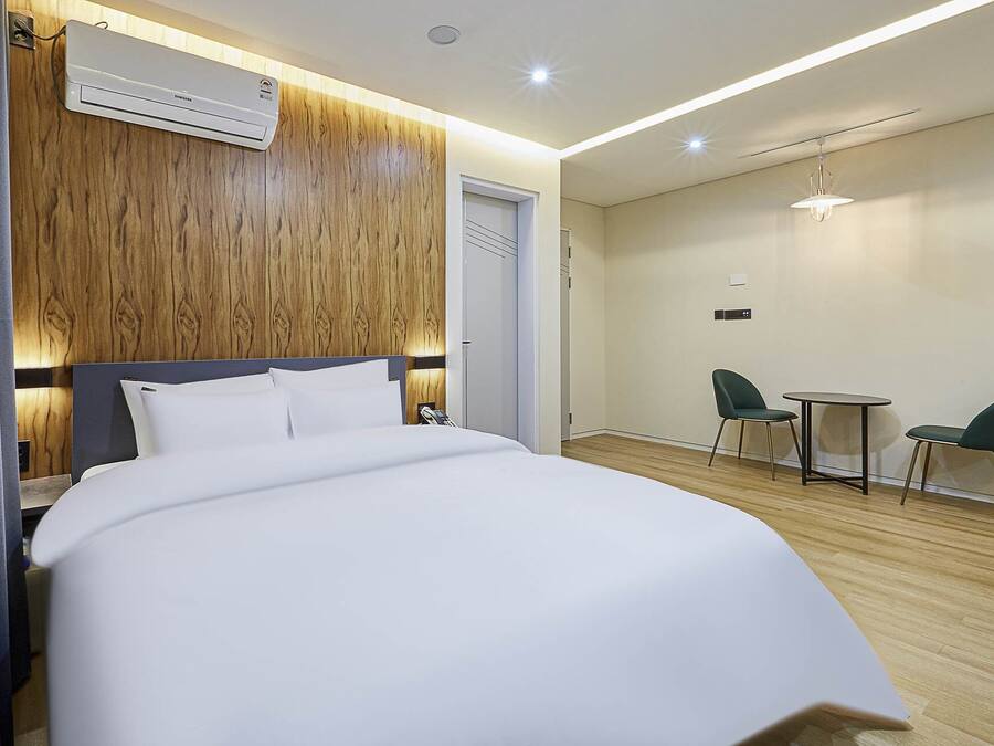 Habitación de hotel con una cama grande, un muro decorativo de madera, una pequeña mesa con dos sillas y una lámpara en el techo.