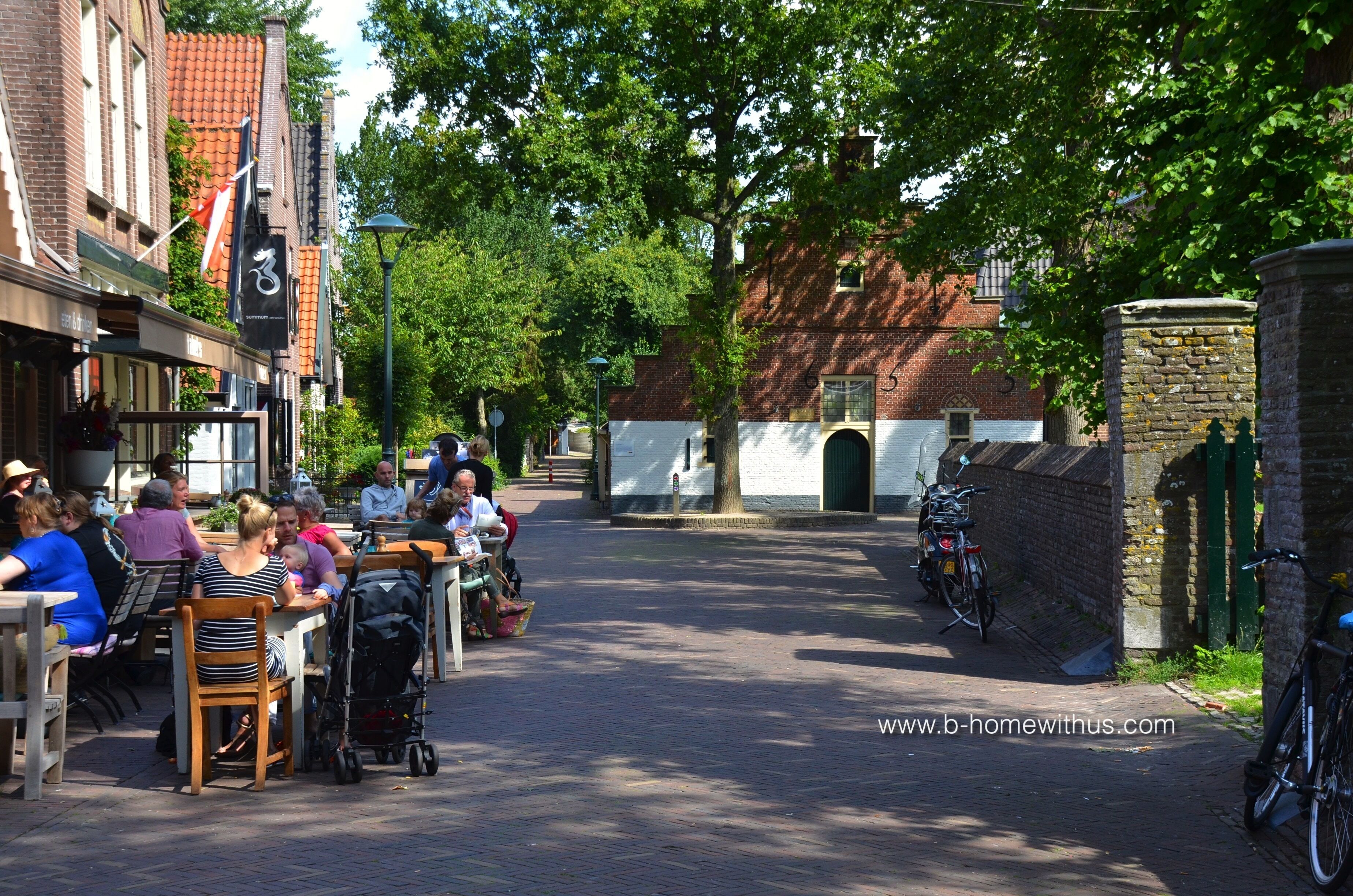 En kullerstensgata kantad av byggnader i tegel, med uteserveringar för caféer och cyklar parkerade längs sidan.