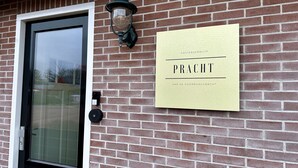 Un mur de briques avec une porte et une enseigne sur laquelle on peut lire : « GASTENVERBLIJF PRACT ».