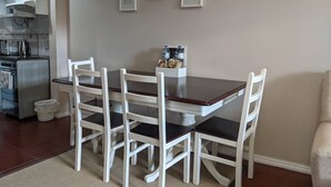 Un comedor con una mesa y cuatro sillas, una cocina equipada y láminas botánicas enmarcadas en la pared.
