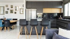 Una cocina moderna con muebles oscuros, una isla central y un comedor con sillas azules y una mesa de madera.