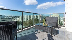 Un balcón con mobiliario de mimbre, una mesa de vidrio y vistas a la ciudad.