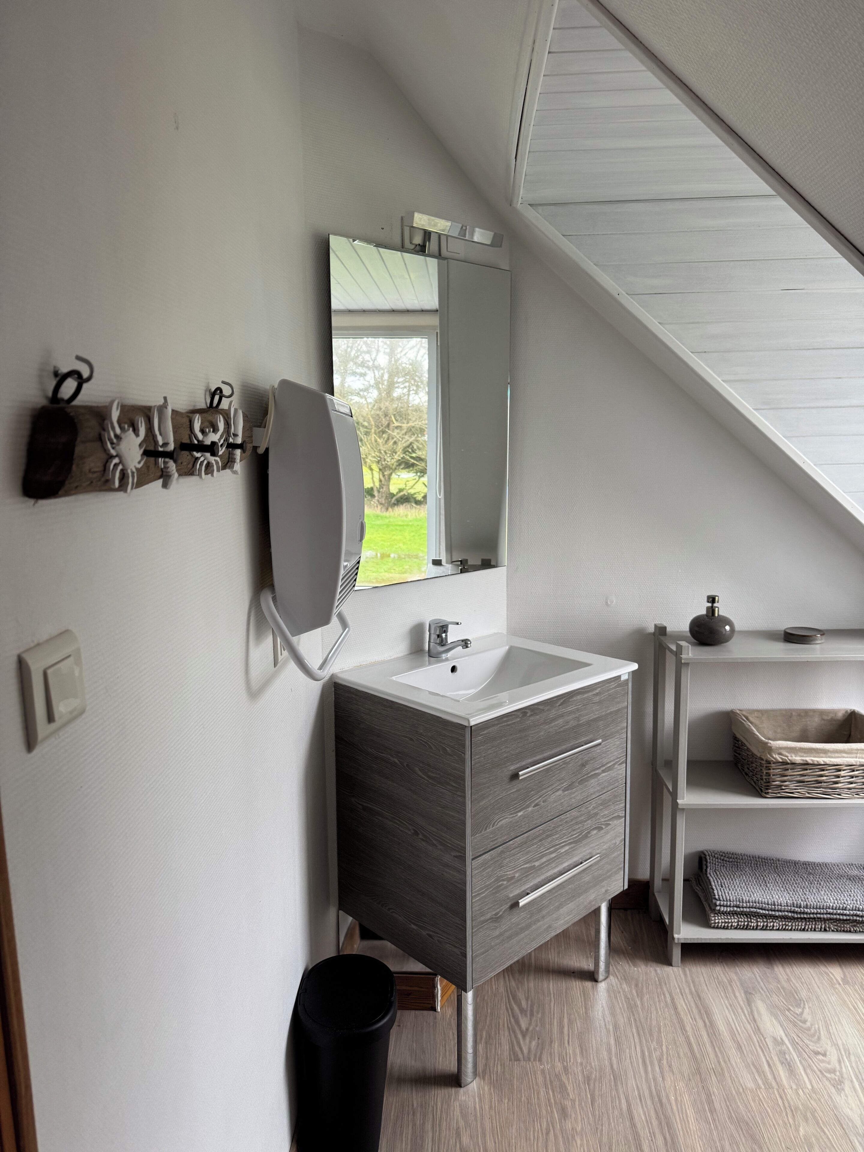 Une salle de bain moderne dotée d’un puits de lumière, d’un grand miroir, d’un lavabo et d’un meuble-lavabo avec des tiroirs.