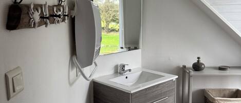Une salle de bain moderne dotée d’un puits de lumière, d’un grand miroir, d’un lavabo et d’un meuble-lavabo avec des tiroirs.