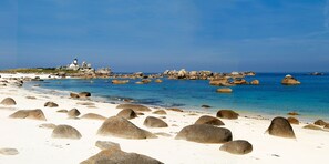Uma praia com pedras grandes e um farol ao fundo.