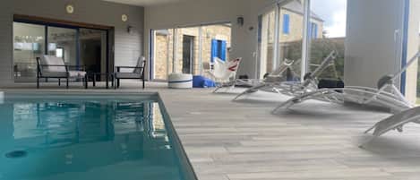 A swimming pool area with lounge chairs and a glass door leading to an outdoor space.