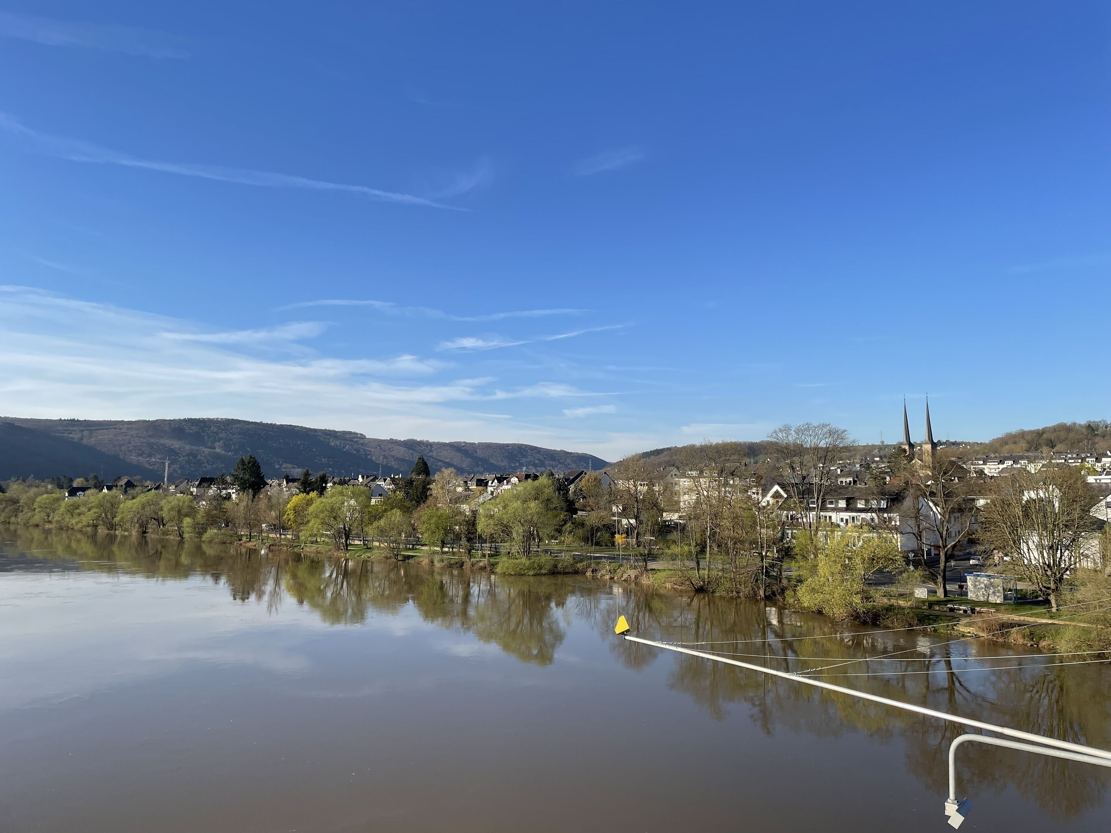 Un lago tranquilo con el reflejo nítido del paisaje circundante, incluyendo la aguja de una iglesia y edificios residenciales.