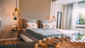 A modern bedroom with a bed, two pendant lights, a bedside table, and a view of greenery outside. - Premium Apartments Koblenz  (Koblenz)