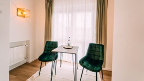 A room with a white radiator, a table with a water bottle, two green chairs, and a wall-mounted light fixture. - Premium Apartments Koblenz  (Koblenz)