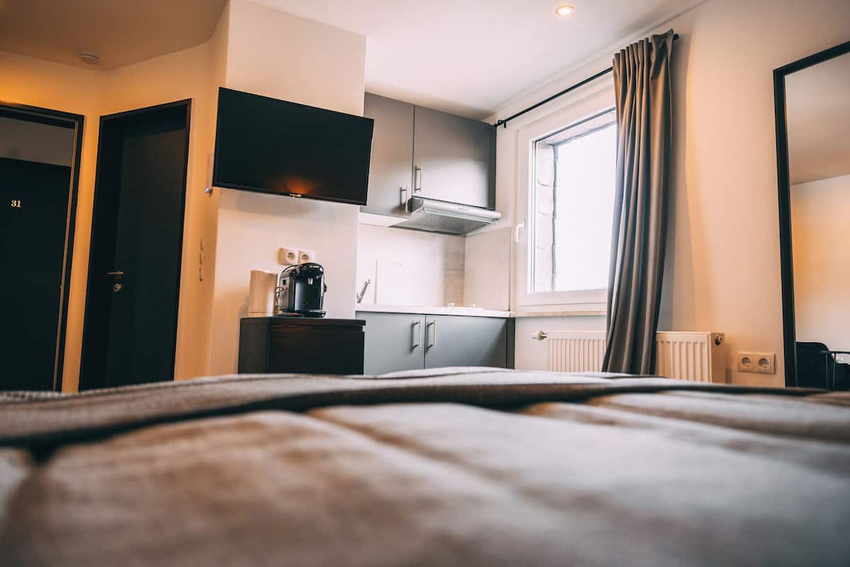 Quarto de hotel com cama, cozinha compacta, televisão e janela com cortinas.