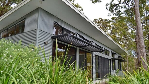 A modern house with a sloped roof, large windows, and a covered porch area.