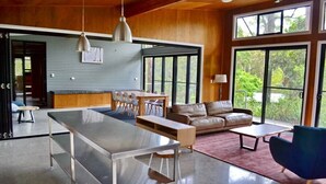 A spacious living area with a large dining table, leather sofa, and a blue armchair.