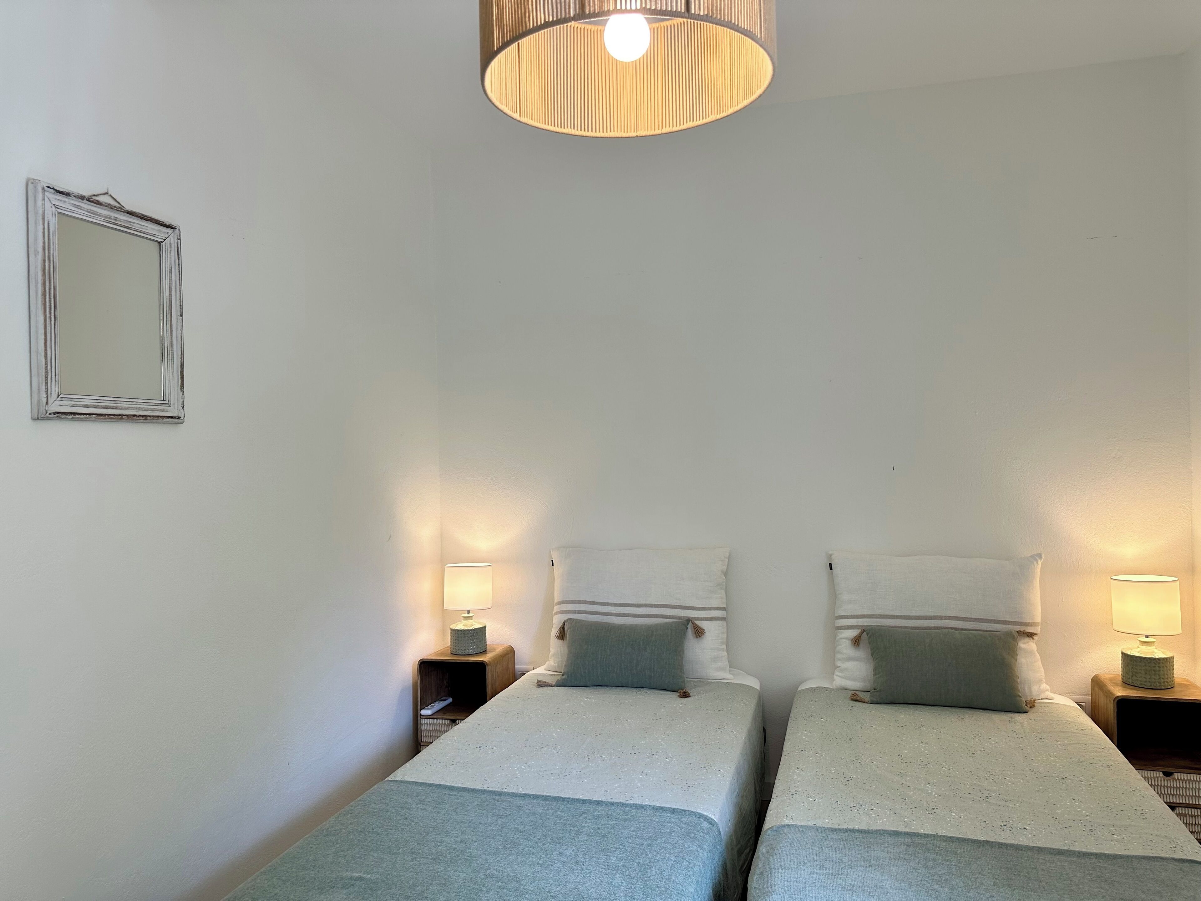 A bedroom with two single beds, each with a nightstand and a lamp. A mirror hangs on the wall to the left.