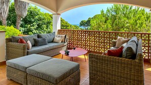 A covered outdoor seating area with wicker furniture and a view of the sea.