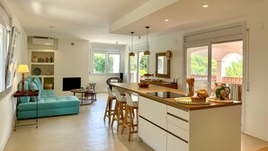 A modern kitchen with a central island, a dining area with a table and chairs, and a living room with a sofa.