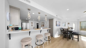 A modern kitchen with a bar area, wooden stools, and a dining table with chairs.
