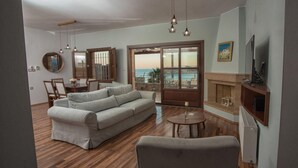 Una sala de estar con sofá, sillón, chimenea y vista al mar a través de un ventanal.