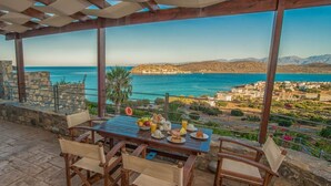 Un área de comedor al aire libre techada, con una mesa dispuesta para el desayuno, con vistas a un paisaje costero.