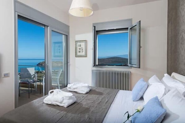Une chambre à coucher avec un lit, une fenêtre donnant sur la mer, une chaise et une table.