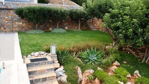 A modern house with a stone exterior, a well-maintained lawn, and a variety of plants.